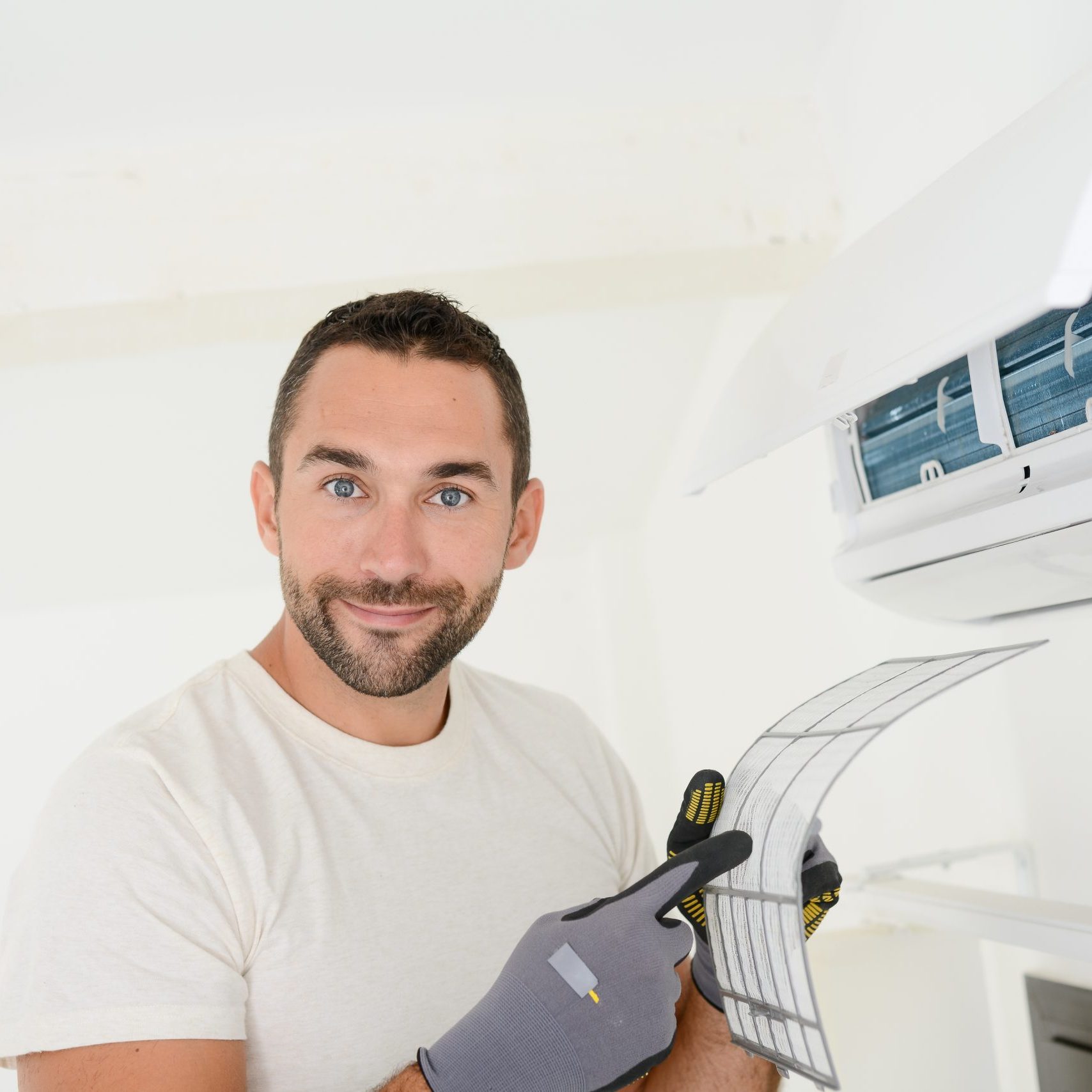 handsome young man electrician cleaning air filter on an indoor unit of air conditioning in a client house